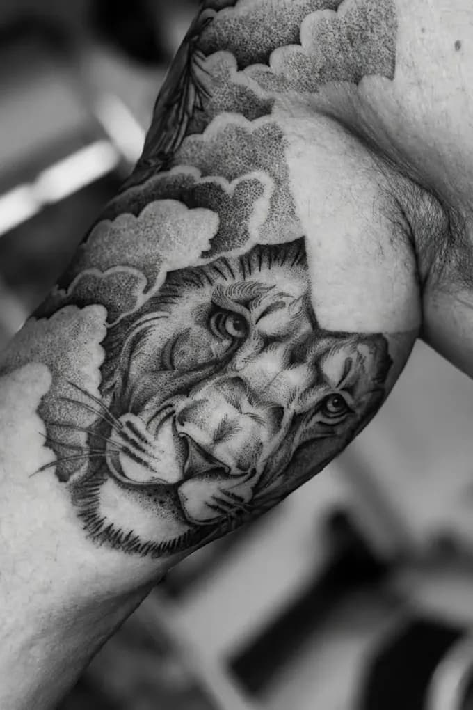 Dotwork lion among clouds, tattooed on an arm