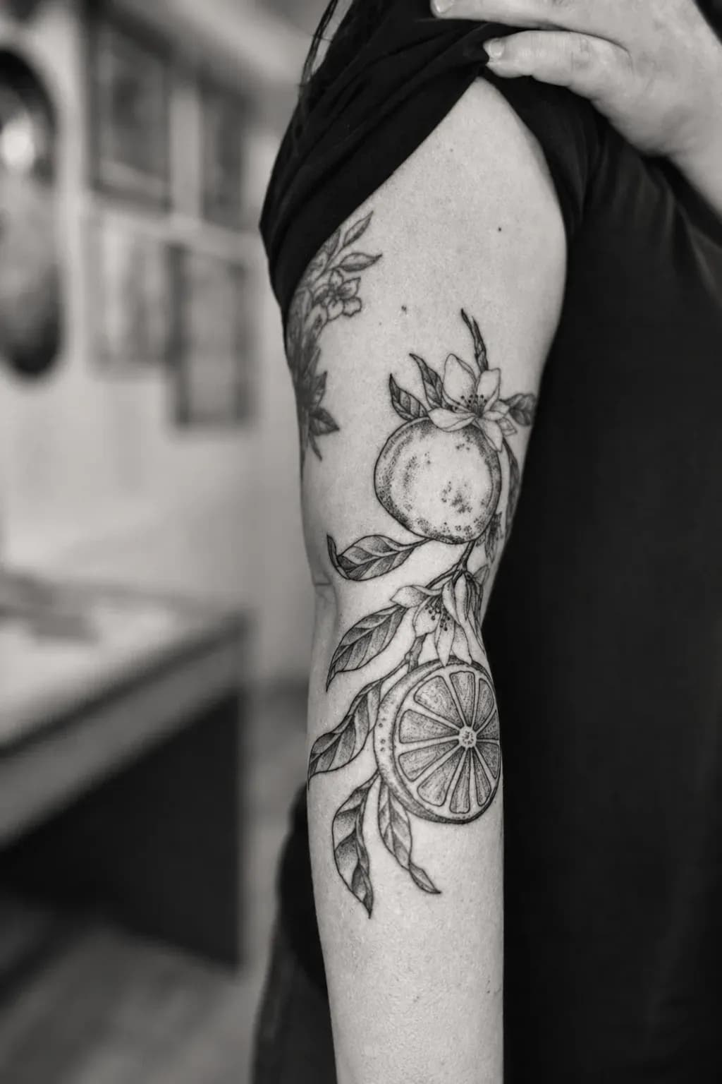 Fine-line orange branch and slice tattooed on an arm