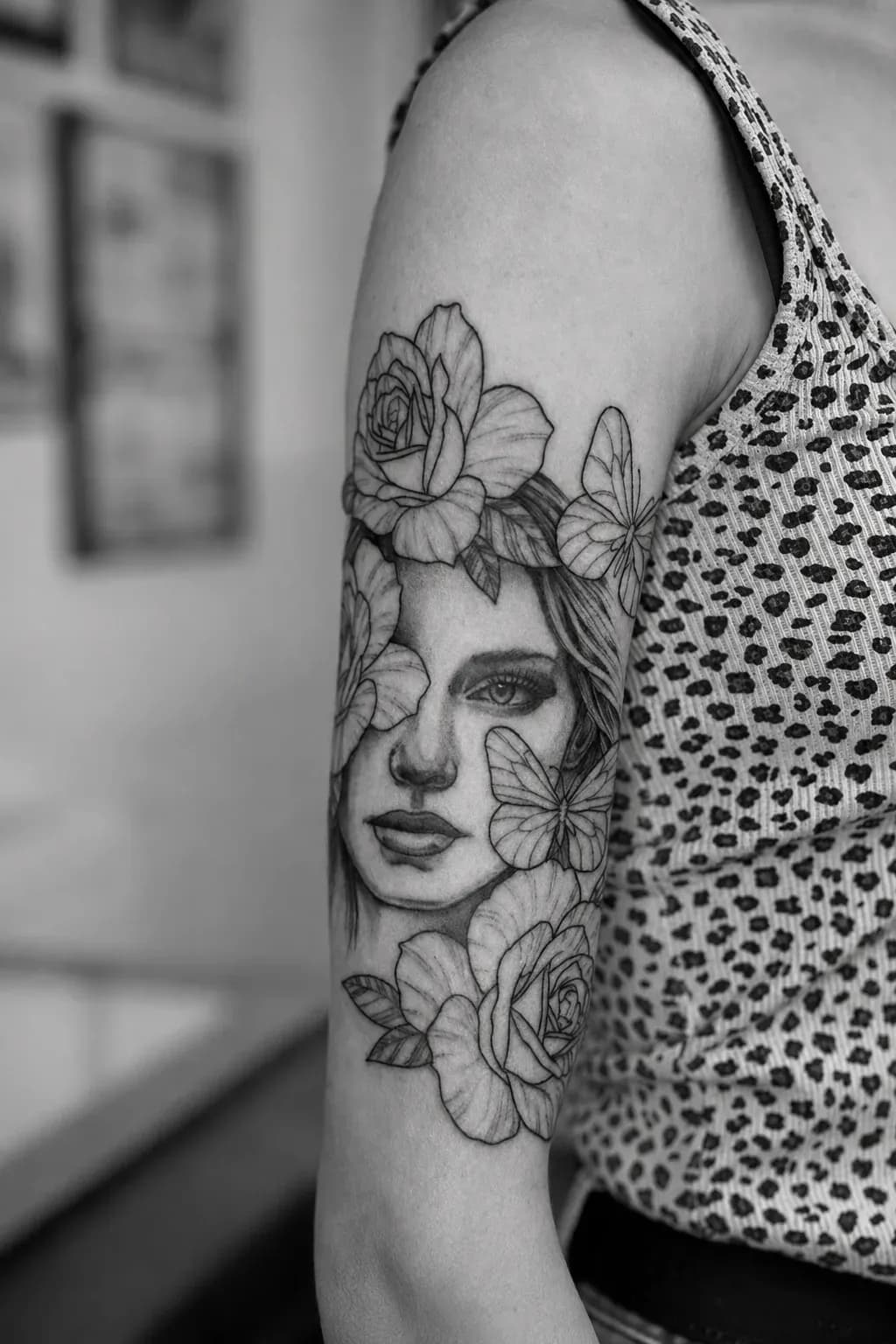 Fine-line portrait with roses and a butterfly, tattooed on an arm